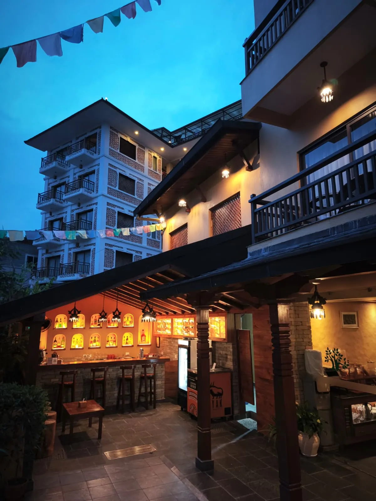 Carved timber pillars and prayer flags at the entrance of Bar Peepal Resort at dusk